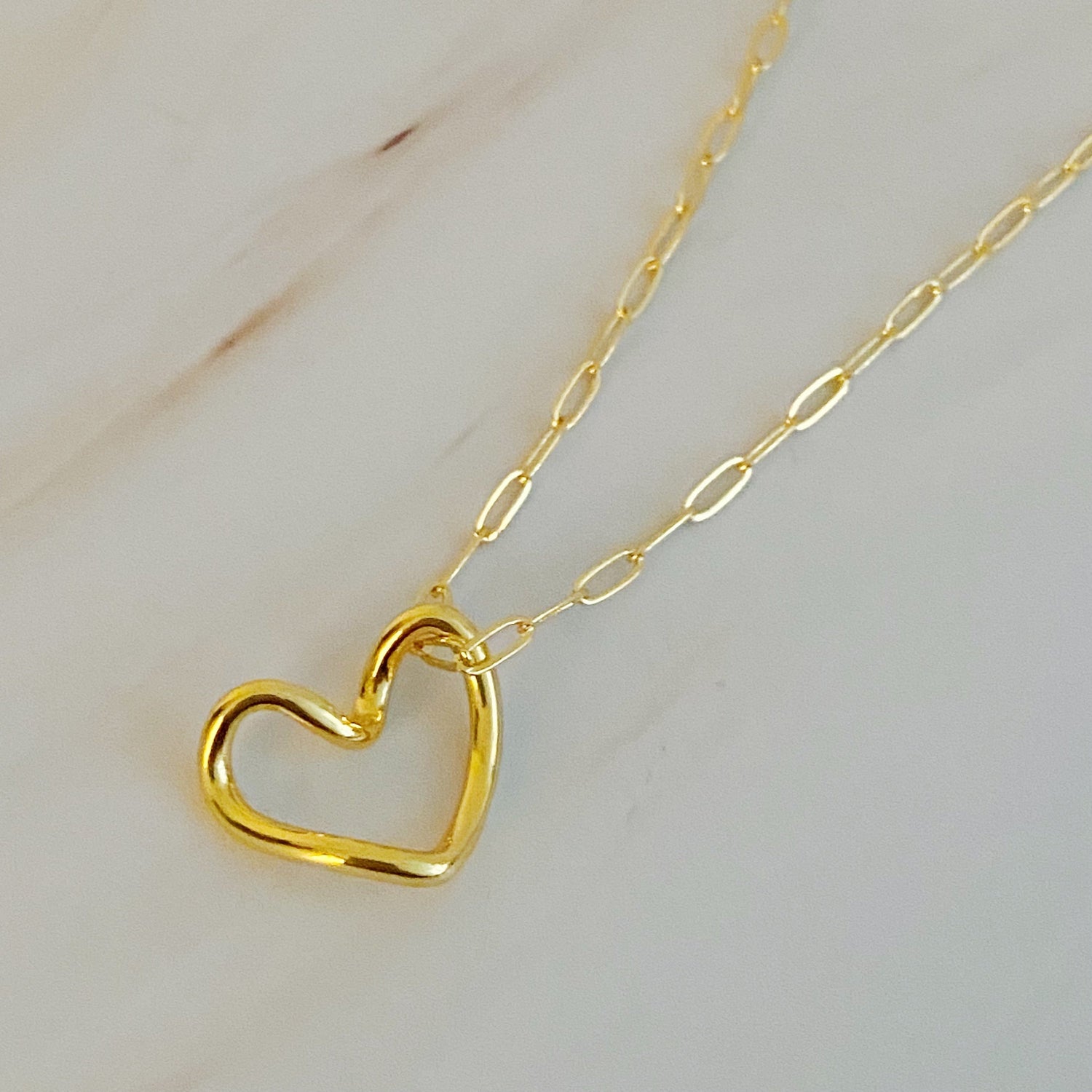 Gold heart-shaped pendant on a delicate chain, displayed on a white marble surface.