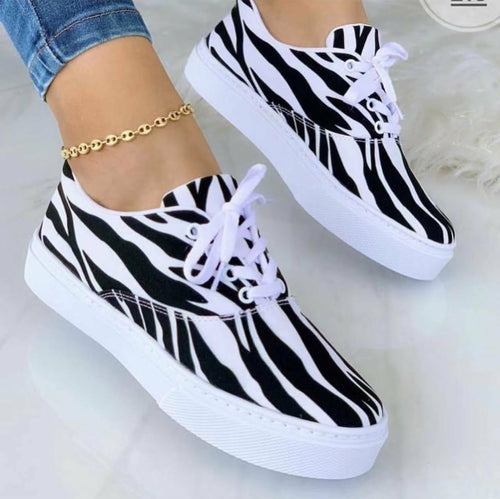 Woman wearing trendy zebra print sneakers with white laces and thick soles, styled with a gold ankle bracelet and jeans.