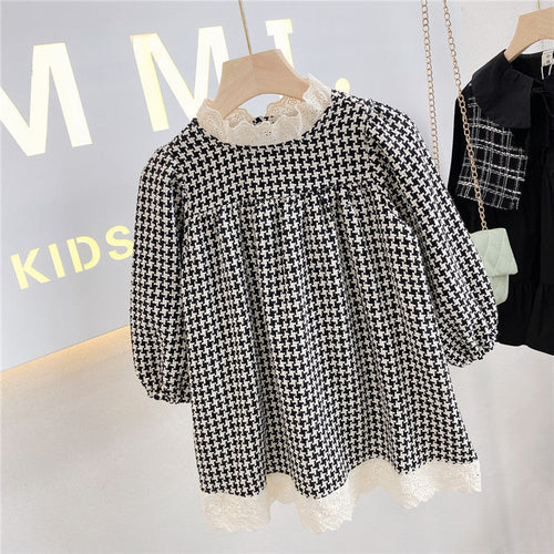 Trendy houndstooth patterned kids' dress with lace hem displayed in a children's clothing store.