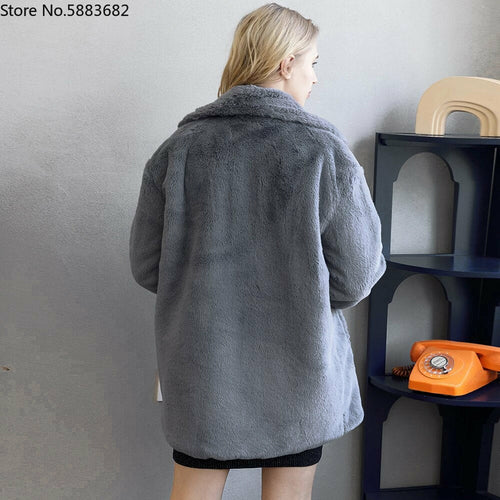 Woman wearing elegant gray faux fur coat, featuring a thick warm material with turn-down collar, viewed from behind in a stylish interior setting.