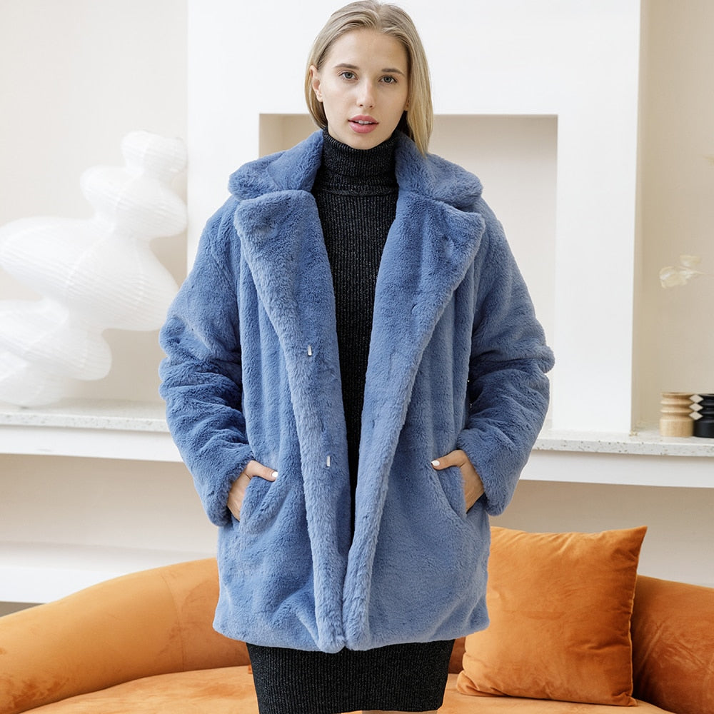 Woman wearing a 2022 Autumn Winter elegant blue faux fur coat, fluffy and thick, standing in a stylish living room.