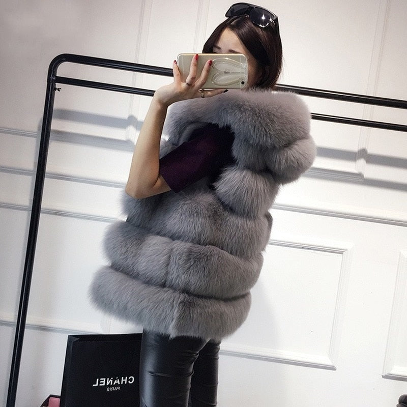 Woman in a stylish 2022 winter sleeveless artificial fox fur gilet with hood, modeling in front of a mirror while taking a selfie.