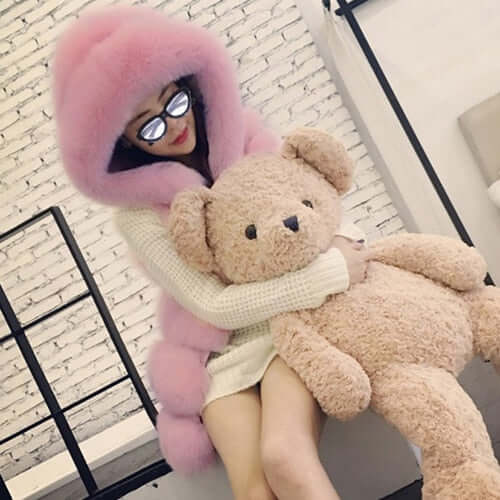 Woman in pink faux fur coat hugging large teddy bear, showcasing stylish winter fashion with a cozy vibe.