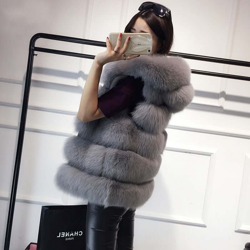 Woman wearing a stylish gray sleeveless faux fur coat with a hood, perfect for winter fashion and warmth.