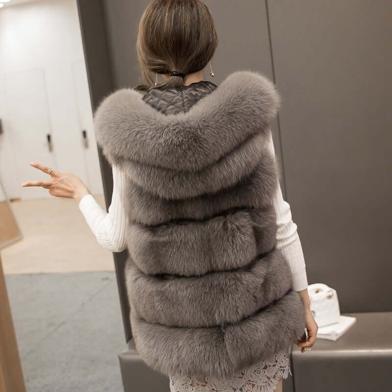 Stylish woman wearing a gray sleeveless faux fur coat with a hood, showcasing a luxurious winter fashion look.