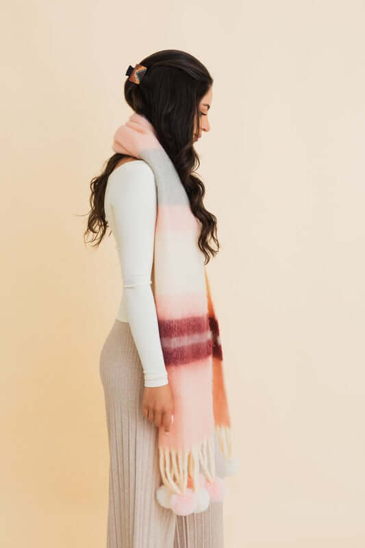 Young woman wearing a Contrast Color Stripes Chunky Pom Tassel Scarf, showcasing bold stripes and playful pom tassels.