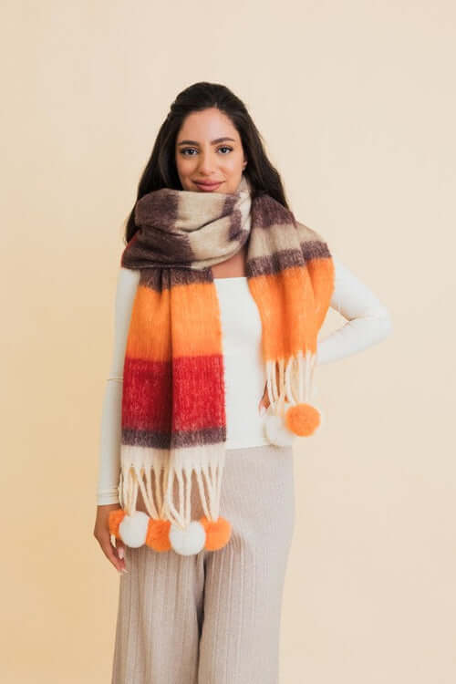 Woman wearing a vibrant Contrast Color Stripes Chunky Pom Tassel Scarf with bold orange and brown hues.