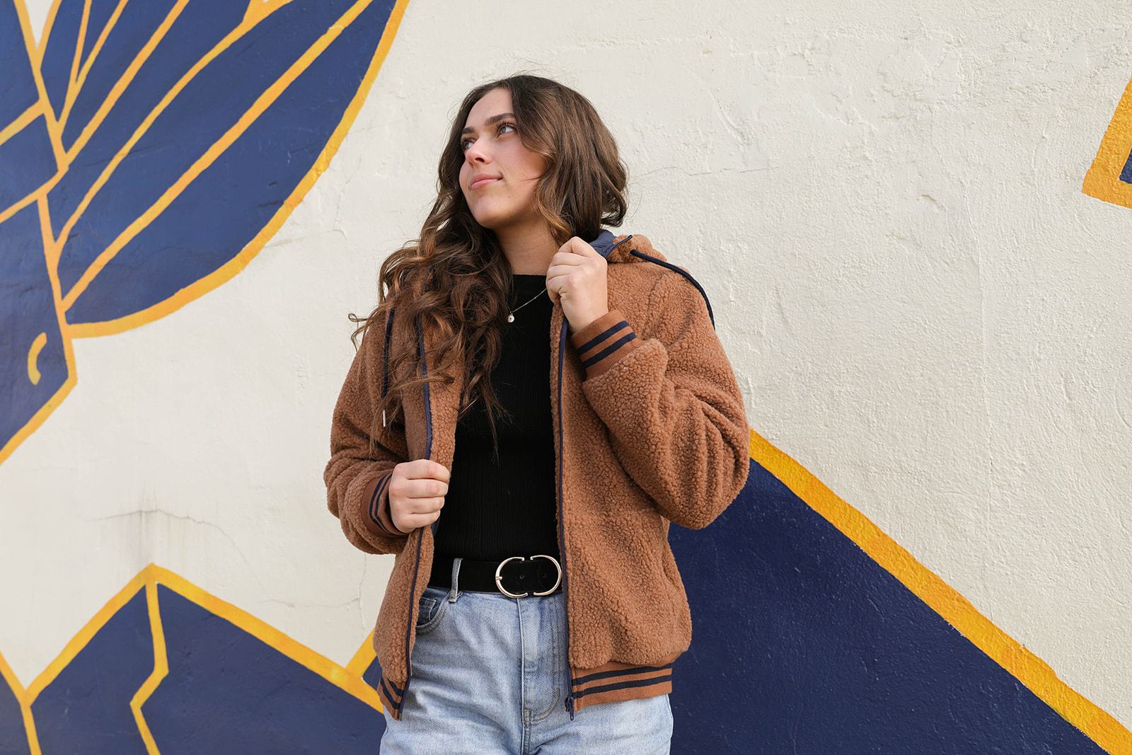 Woman wearing DT Bode Sherpa Winter Jacket in Brown, standing against a mural wall.