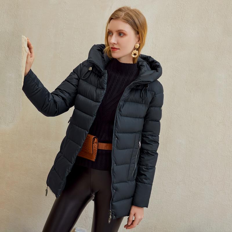 Woman wearing a warm hooded winter coat, casual parkas jacket in black, with stylish leather pants and gold earrings, posing against a neutral background.