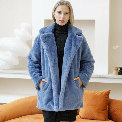 Woman in elegant blue faux fur coat, standing in a stylish interior with orange sofa, winter 2022 fashion