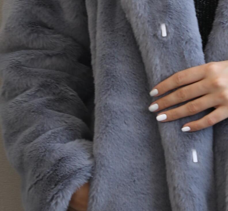 Close-up of a woman's hand with white manicure on a fluffy gray faux fur coat, highlighting elegant texture and stylish design.