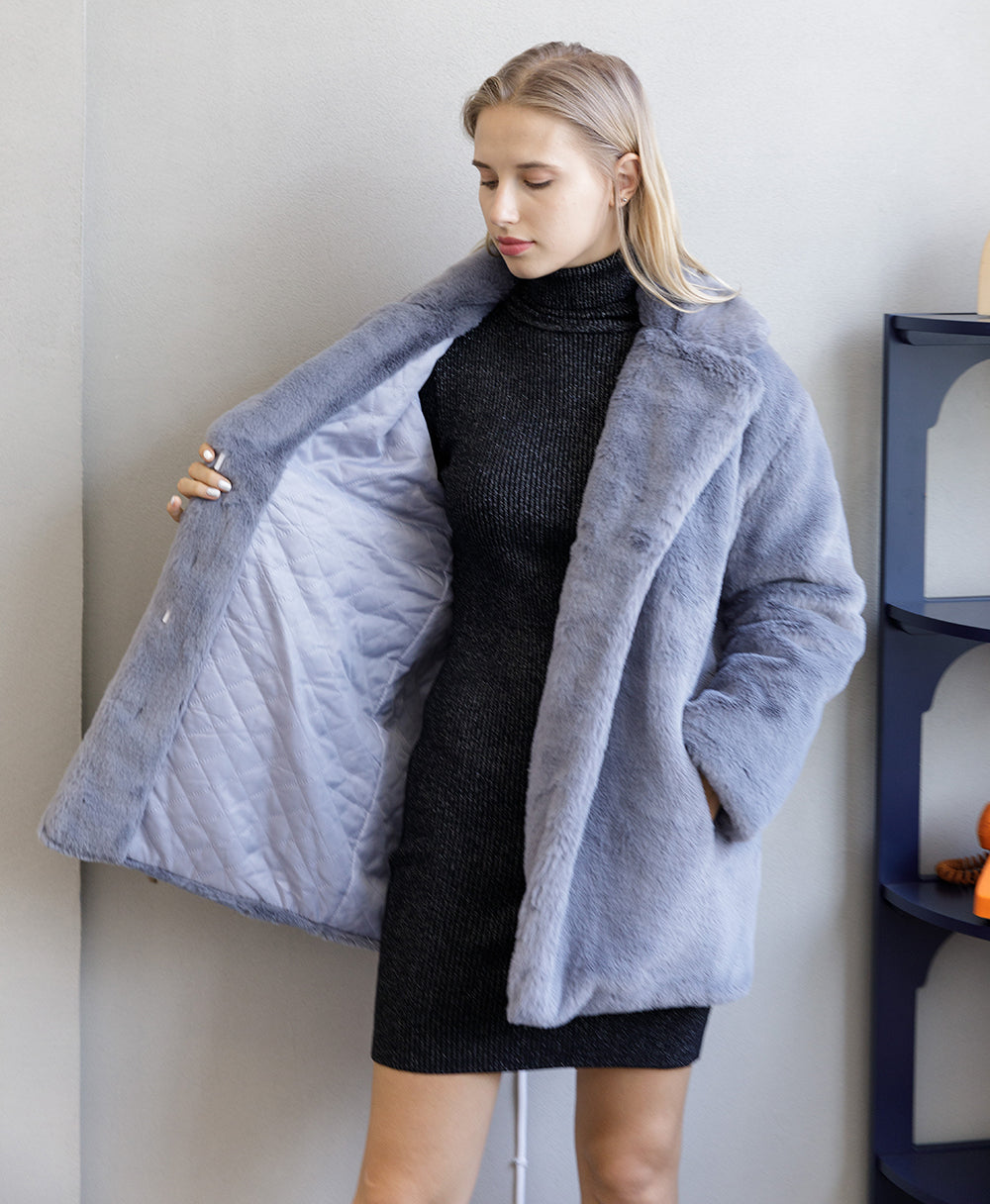 Woman in elegant gray faux fur coat with turn-down collar, showcasing the thick lining, paired with a black knit dress.