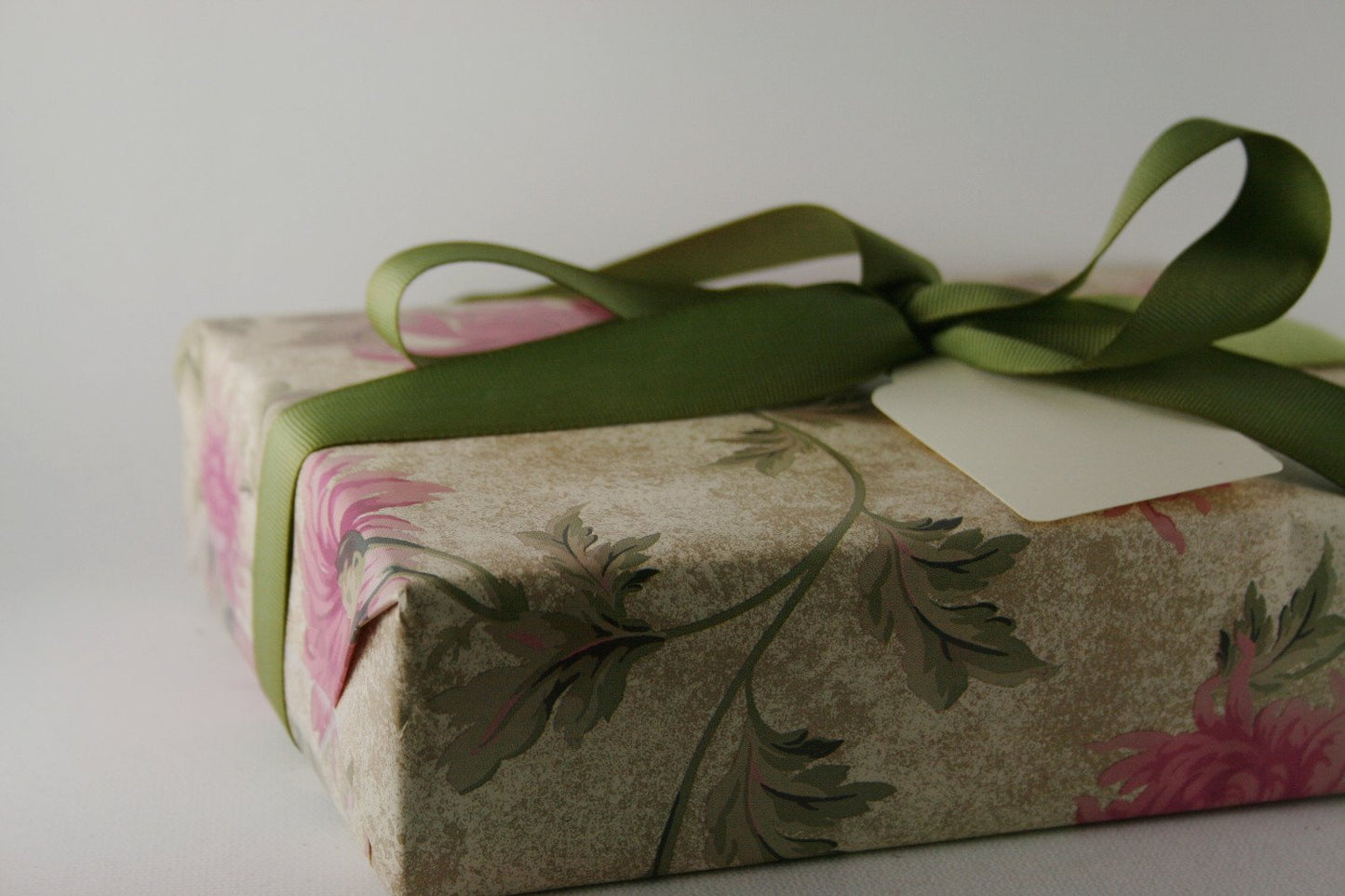 Elegantly wrapped gift box with green ribbon and blank gift tag, featuring floral print on light background, ideal for special occasions