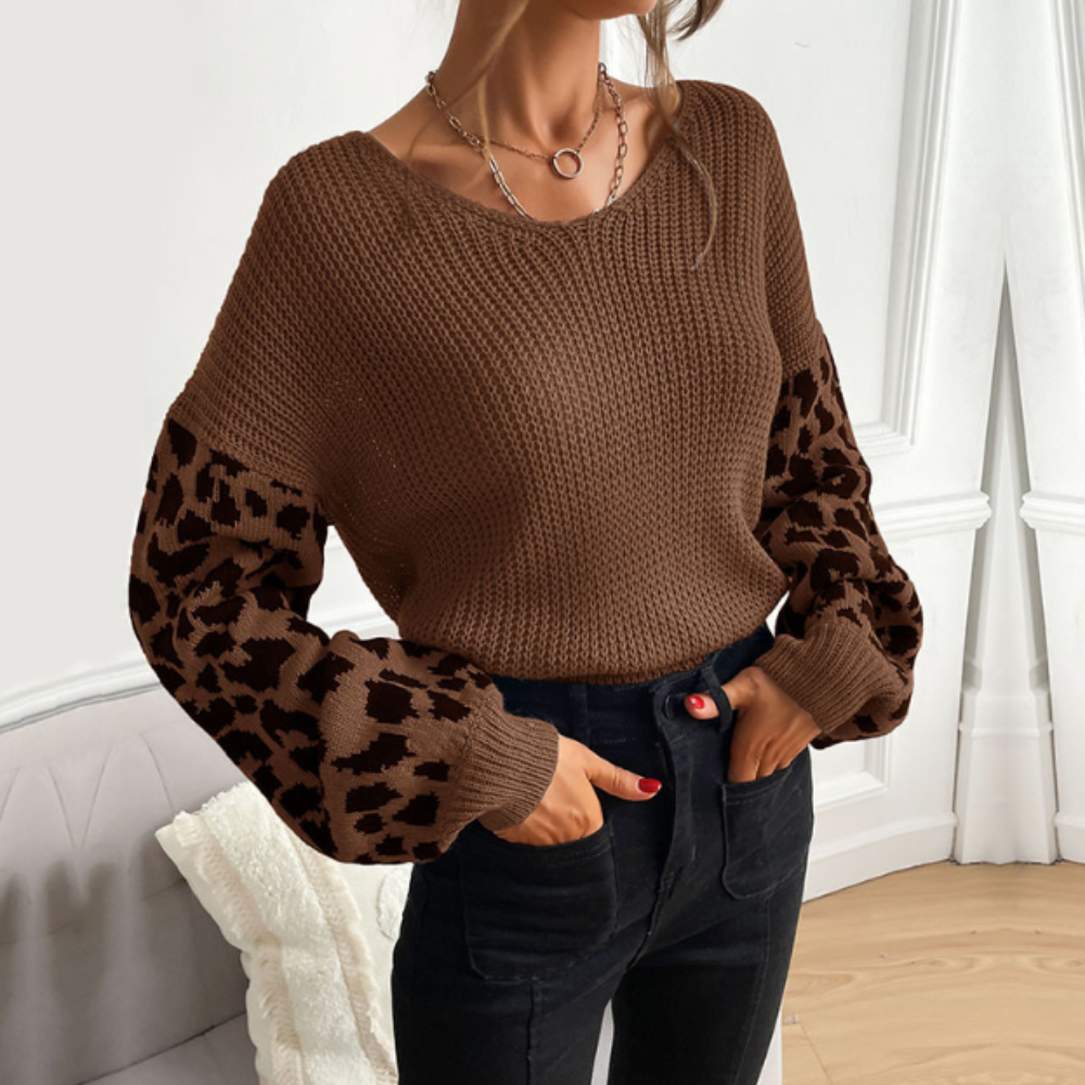 Woman wearing a brown V-neck sweater with leopard print sleeves styled with blue jeans and chic necklaces