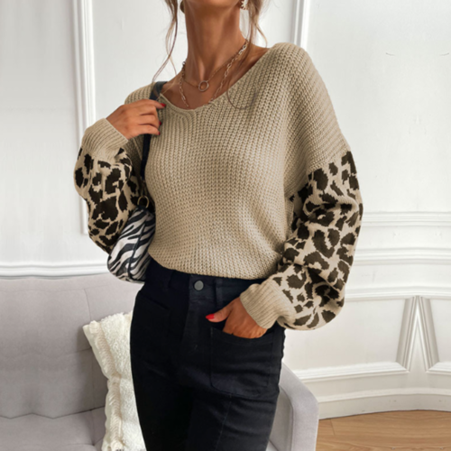 Woman wearing a beige V-neck sweater with leopard print sleeves, paired with dark jeans, stylish in a chic home setting.