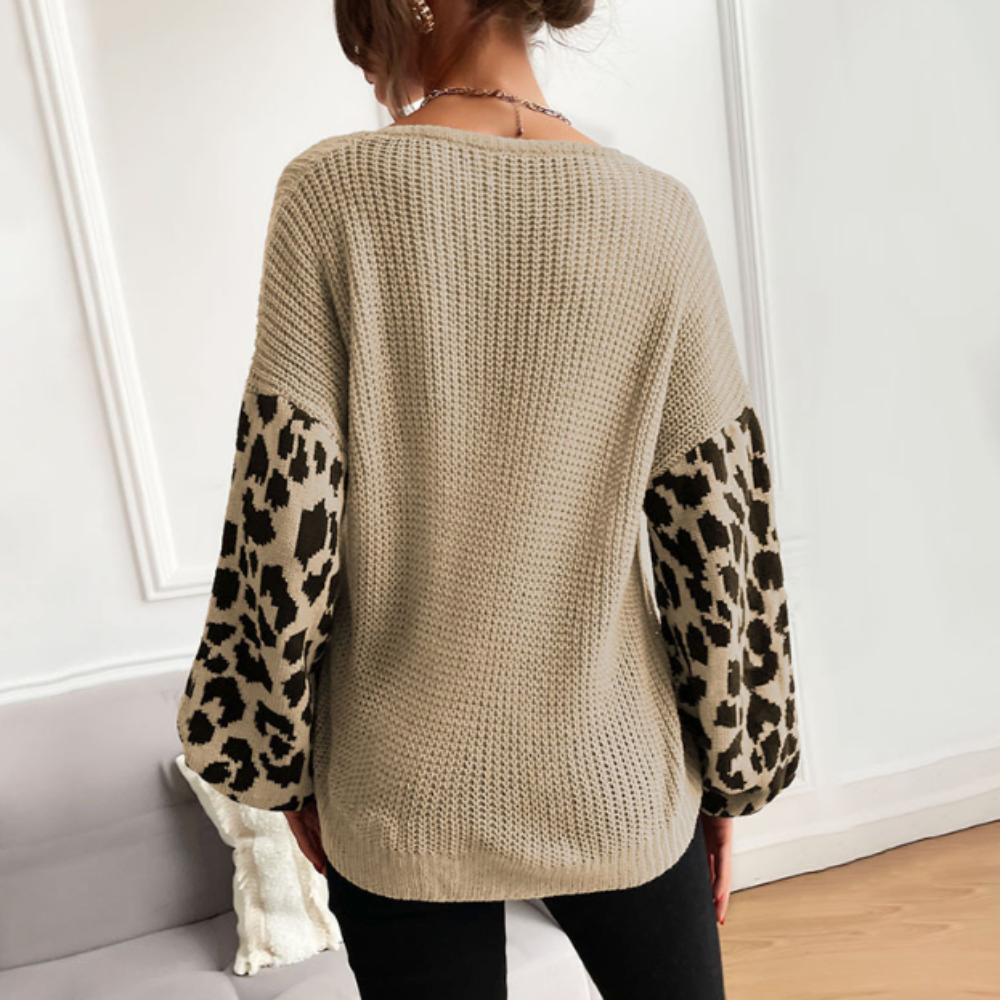 Woman wearing a beige V-neck sweater with leopard print sleeves, viewed from the back in a stylish indoor setting.