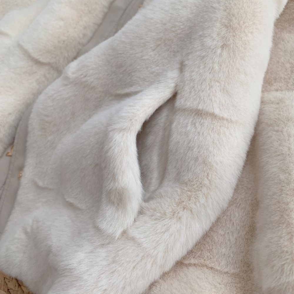 Close-up of a women's faux fur jacket with vegan leather trimmed cuffs in soft white tones.