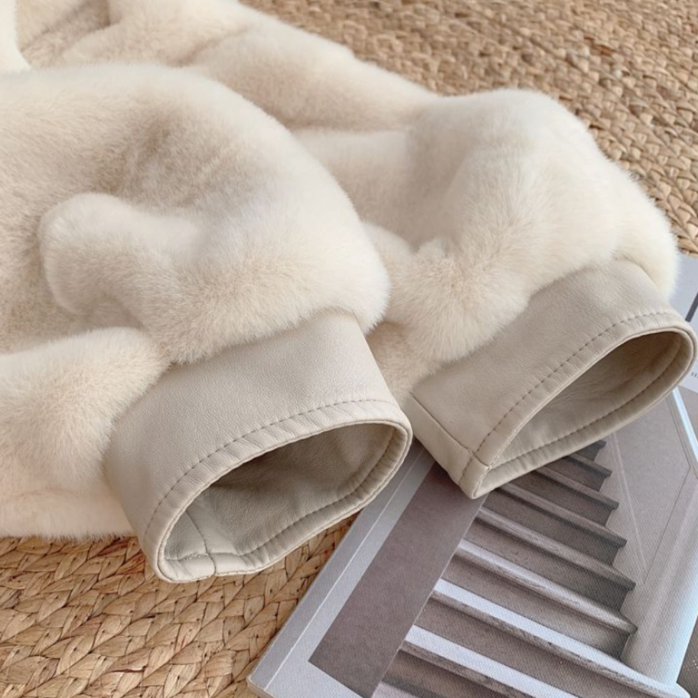 Close-up of a women's faux fur jacket with vegan leather trimmed cuffs on a woven mat next to a magazine.