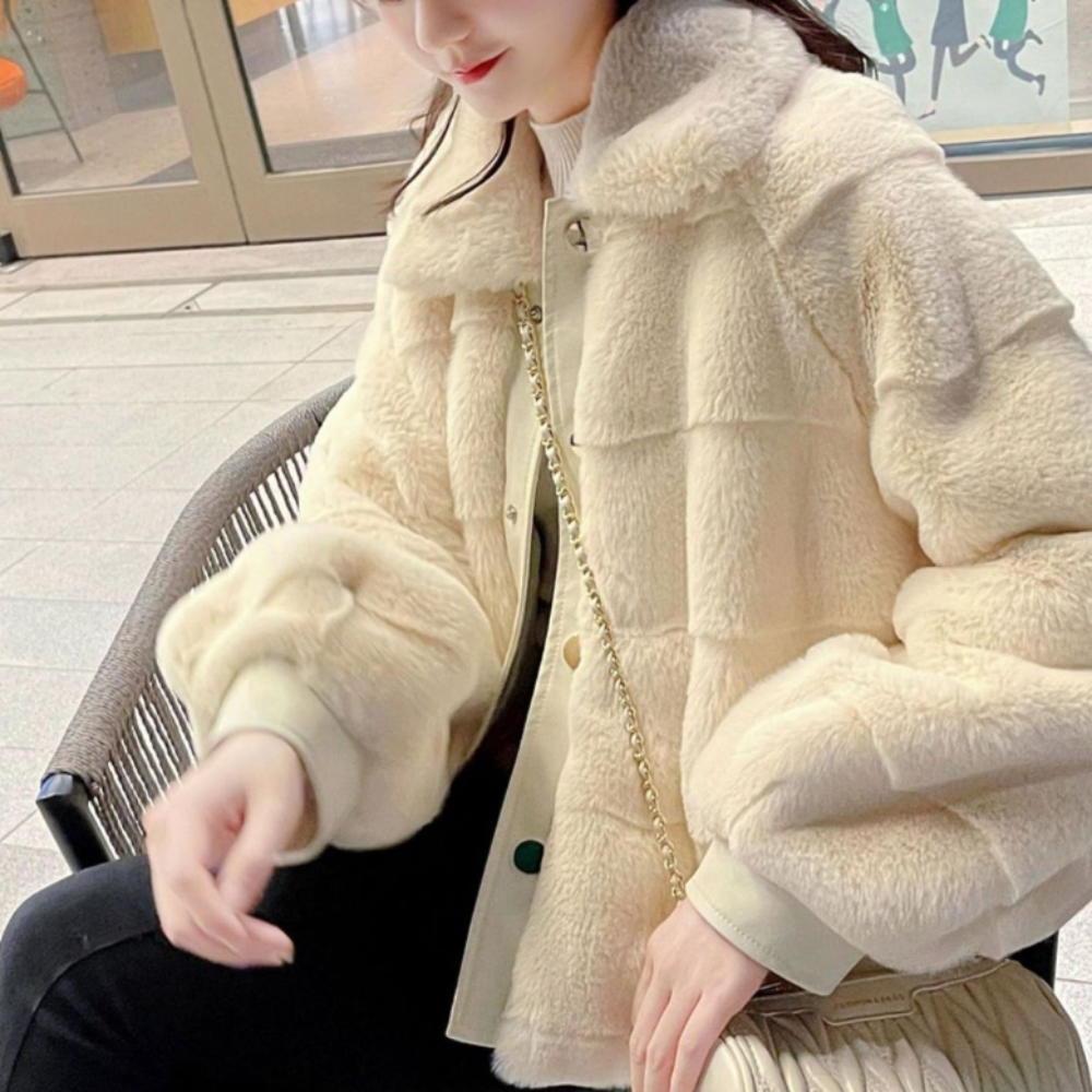 Woman seated in mall wearing stylish faux fur jacket with vegan leather trimmed cuffs and gold chain purse