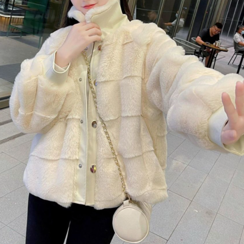 Woman in stylish faux fur jacket with vegan leather trimmed cuffs, accessorized with a small white round purse, posing outdoors.