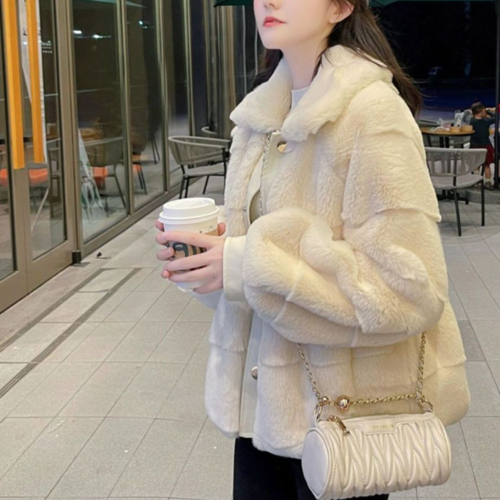 Woman in stylish faux fur jacket with vegan leather trimmed cuffs holding a coffee cup near a café.