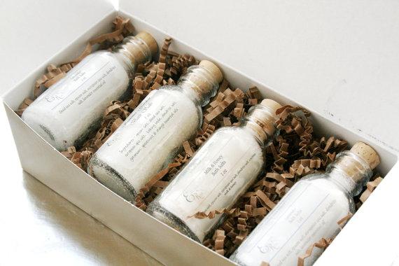 Gold gift box containing four bath salt bottles labeled Lavender Mint Splash, Winter Calm, Grapefruit, and Muscle Therapy, nestled in crinkled paper.