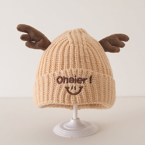 Beige knitted baby hat with cute deer antlers and embroidered smiling face on display stand, from the Winter and Autumn collection.