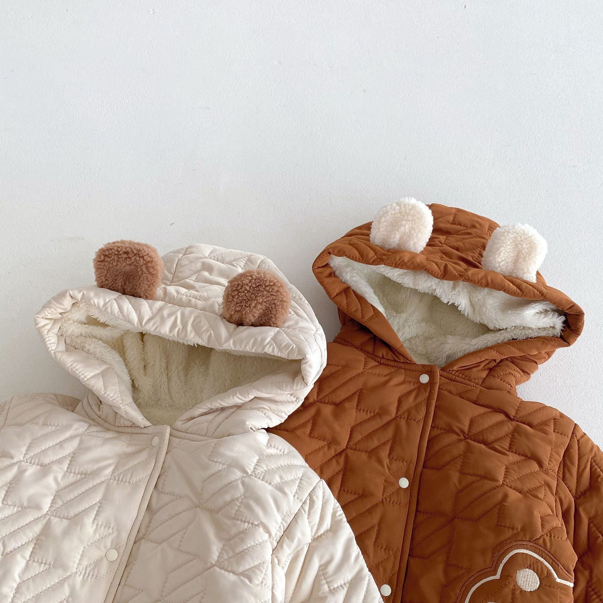 Two winter infant teddy paws pattern coats with hoods, one in white and one in brown, displayed on a plain background.