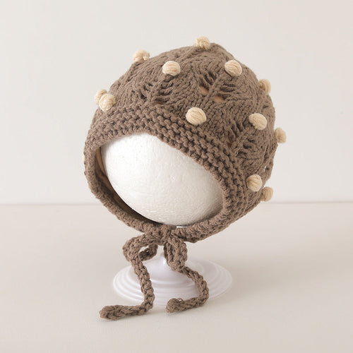 Vintage design brown baby balaclava with cute white pom-poms displayed on a white stand.