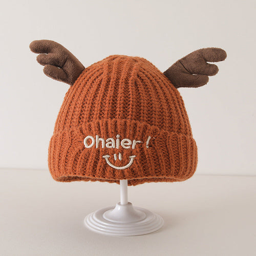 Orange knit baby hat with cute deer antlers and embroidered smiling face, displayed on a white stand