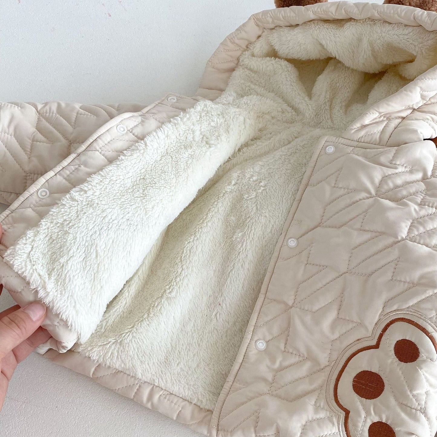 Close-up view of a beige winter infant coat with teddy paws pattern and soft white lining, focusing on texture and details.