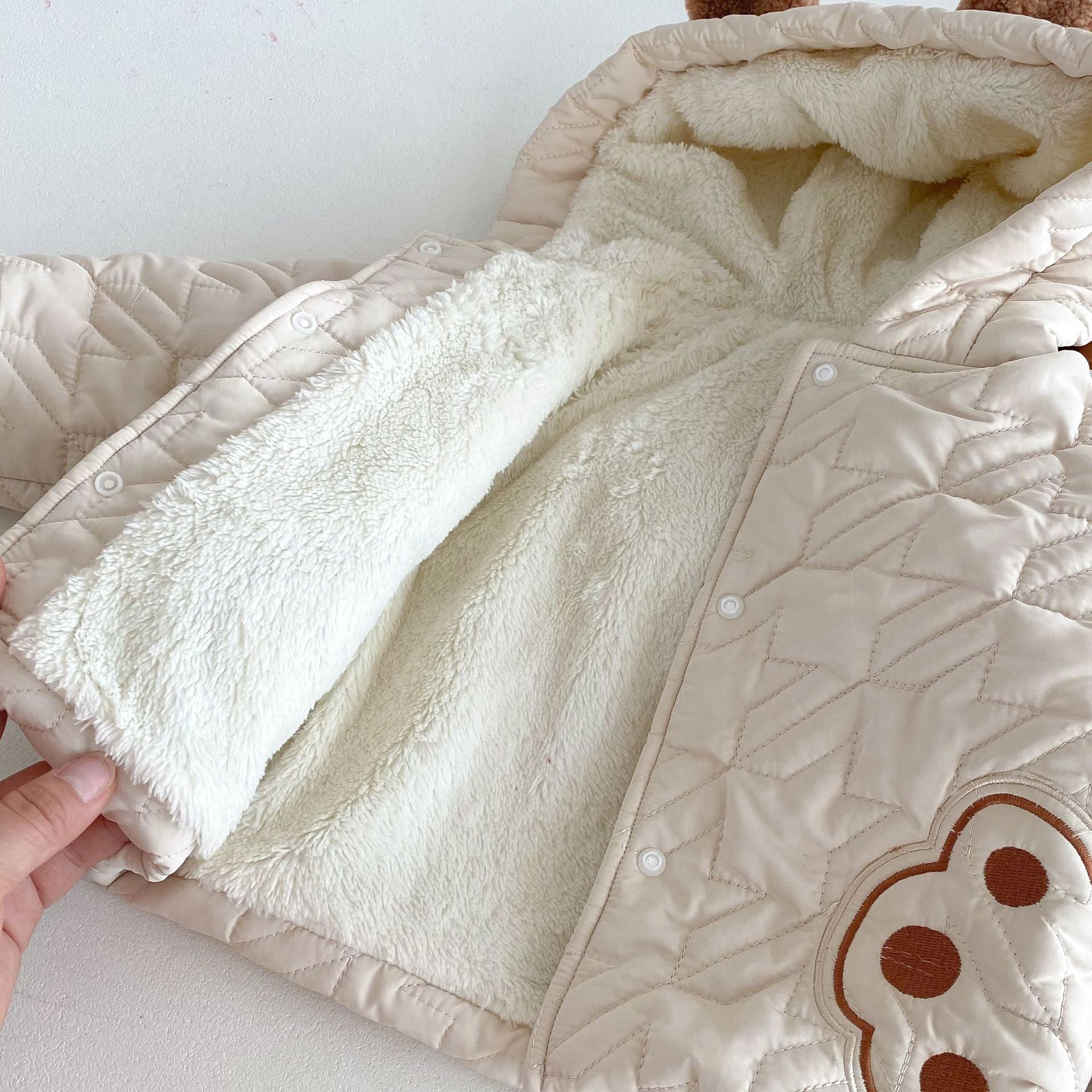 Close-up view of a beige winter infant coat with teddy paws pattern and soft white lining, focusing on texture and details.