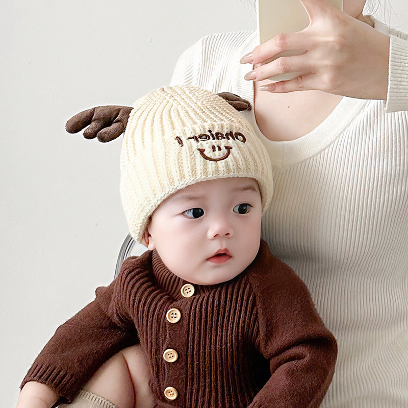 Baby wearing a beige Cute Deer Antlers Knit Hat and brown cardigan, looking adorable and cozy