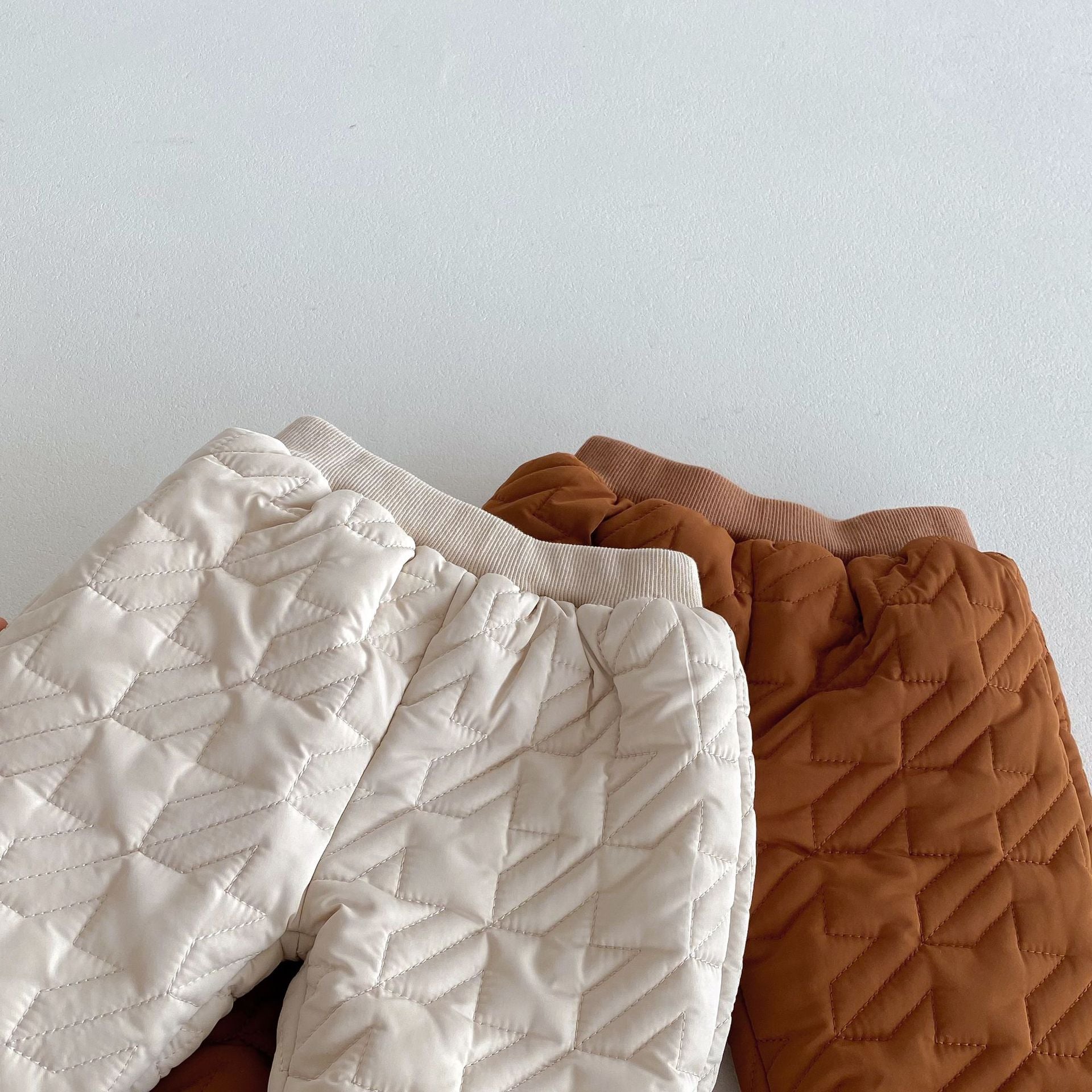 Quilted infant pants in white and brown on white background, designed for warmth and style in chilly weather.