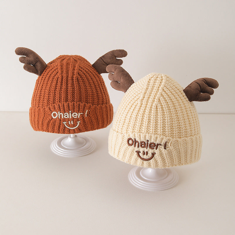 Two cute deer antlers knit hats for babies in orange and beige, displayed on stands with embroidered smiles.