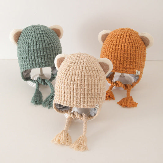 Three colorful baby balaclavas in beige, orange, and green, each with cute ear details and tassels, displayed on a neutral background.